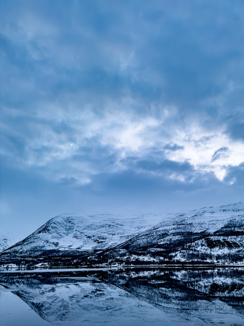Felsiger hoher Berg mit Schnee, der sich im Fjord darunter spiegelt.